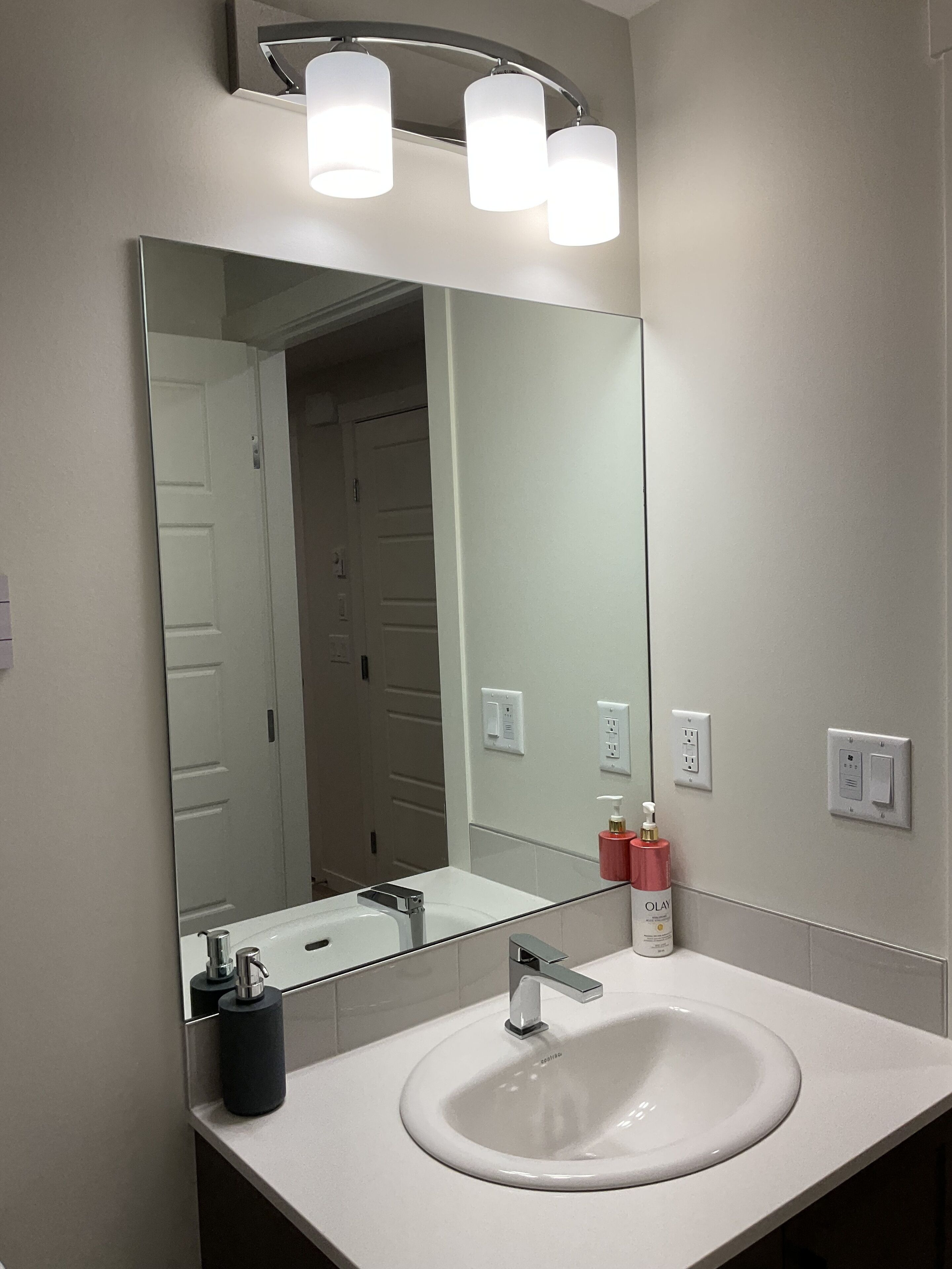 A modern bathroom with a white sink, a large mirror, and a wall-mounted light fixture.