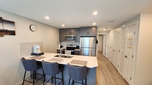 Una cocina moderna con una isla central, taburetes de bar, microondas, refrigerador y un reloj en la pared.