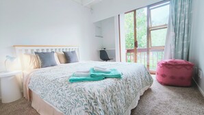A bedroom with a bed, bedside table, lamp, chair, and a window with curtains.