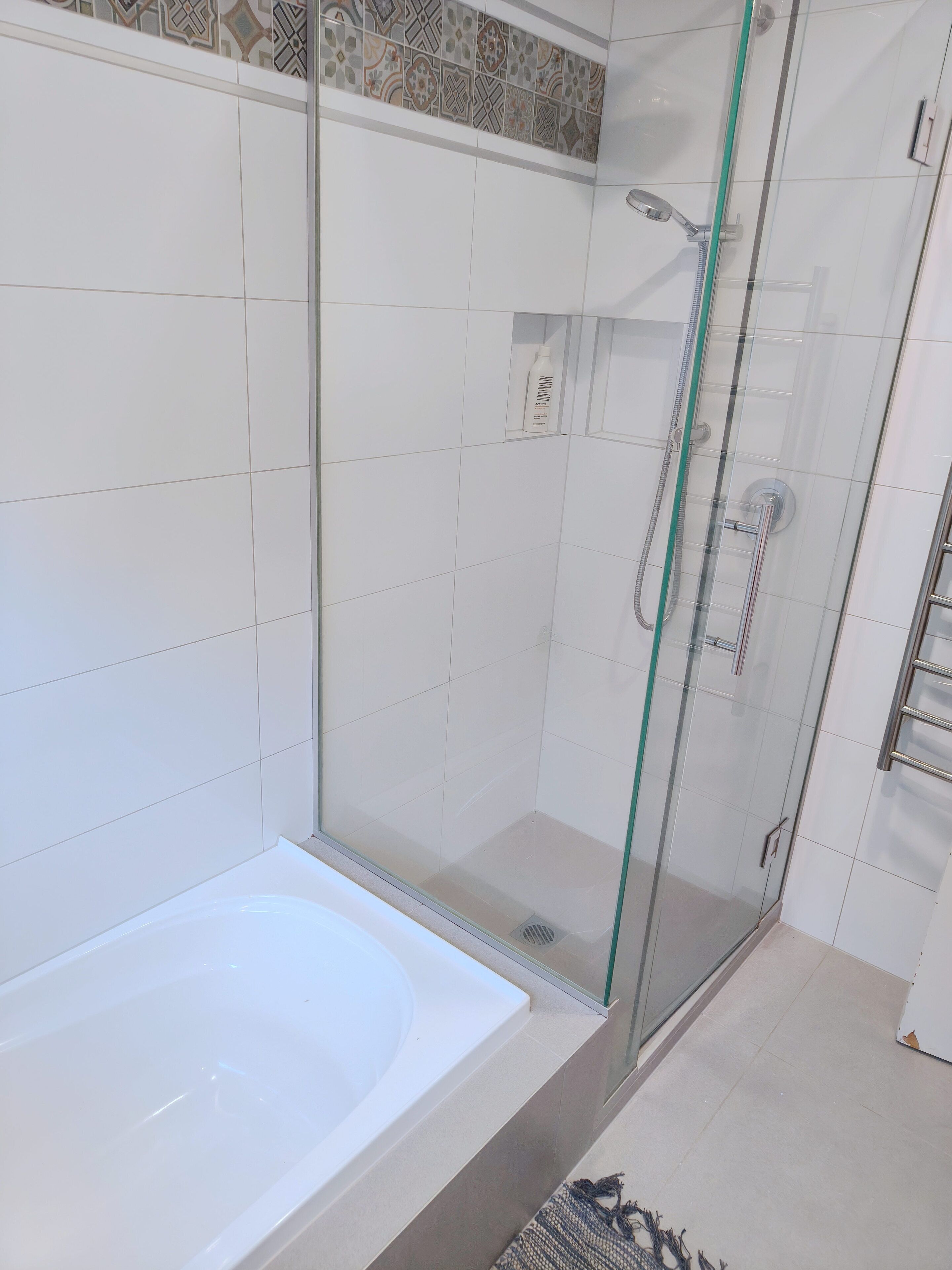 A bathroom with a glass-enclosed shower, a white bathtub, and tiled walls.