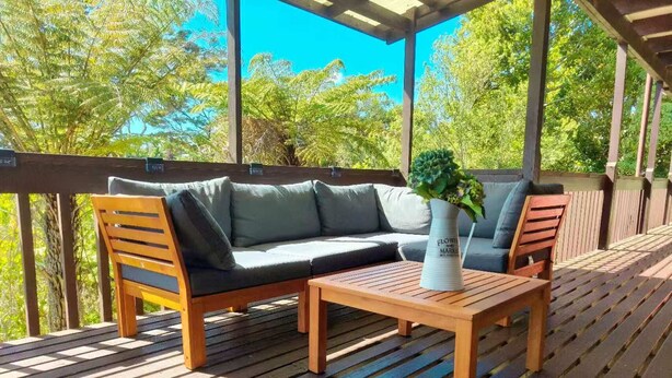 A wooden deck with a sofa and chairs, a table, and a vase with flowers.