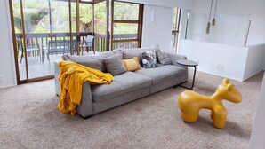 A modern living room with a grey sofa, yellow throw blanket, and a yellow animal-shaped stool.