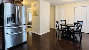 A modern kitchen with a stainless steel refrigerator, wooden cabinets, and a dining area with a table and chairs. - A 3-Bedroom Cozy Cottage - 2 Blocks from the River (Colonial Beach)