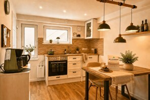 A compact kitchen with a stove, oven, and sink, a dining area with a table and chairs, and a window with a view.