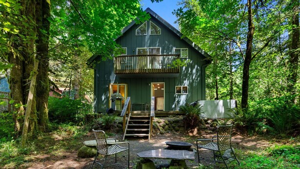 A two-story house with a balcony, surrounded by dense forest. - Wildwood  Cabin in Welches (Mount Hood Village)