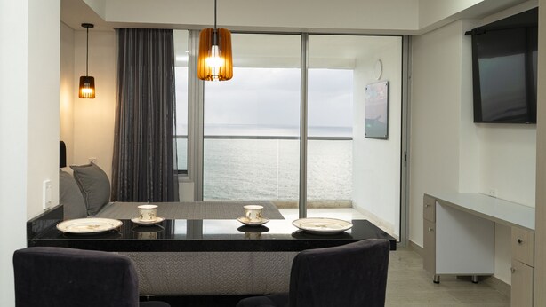 A modern dining area with a large window overlooking the sea, a flat-screen TV mounted on the wall, and a minimalist design. - Loft Apartment 1510 (Cartagena de Indias)