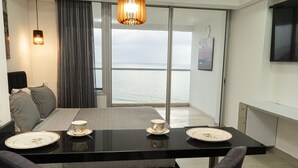 A modern hotel room with a balcony, a dining area with a table set for two, and a bed with a view of the sea. - Loft Apartment 1510 (Cartagena de Indias)