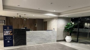 Un espace d’accueil d’hôtel avec un comptoir en marbre, une grande plante en pot et un panneau indiquant « SMDC Good Stays ».