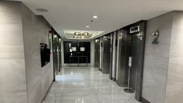 Un couloir moderne avec un plancher poli, un lustre central et des ascenseurs de part et d’autre.