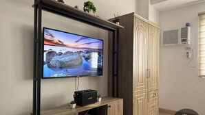 Un salon moderne doté d’un téléviseur à écran plat fixé sur un meuble en bois, d’un climatiseur intégré et d’une armoire en bois.