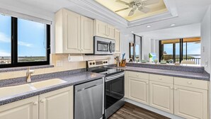 A modern kitchen with white cabinets, a granite countertop, stainless steel appliances, and a view of the ocean through large windows.