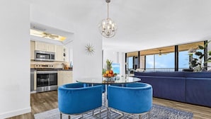 A modern kitchen with white cabinets, stainless steel appliances, and a blue dining area with two chairs and a glass table.