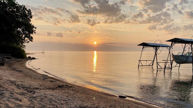 En strand med et roligt hav, en solnedgang og en båd fortøjet til højre.