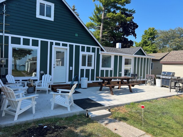 A green building with white trim, outdoor seating, and a barbecue area.