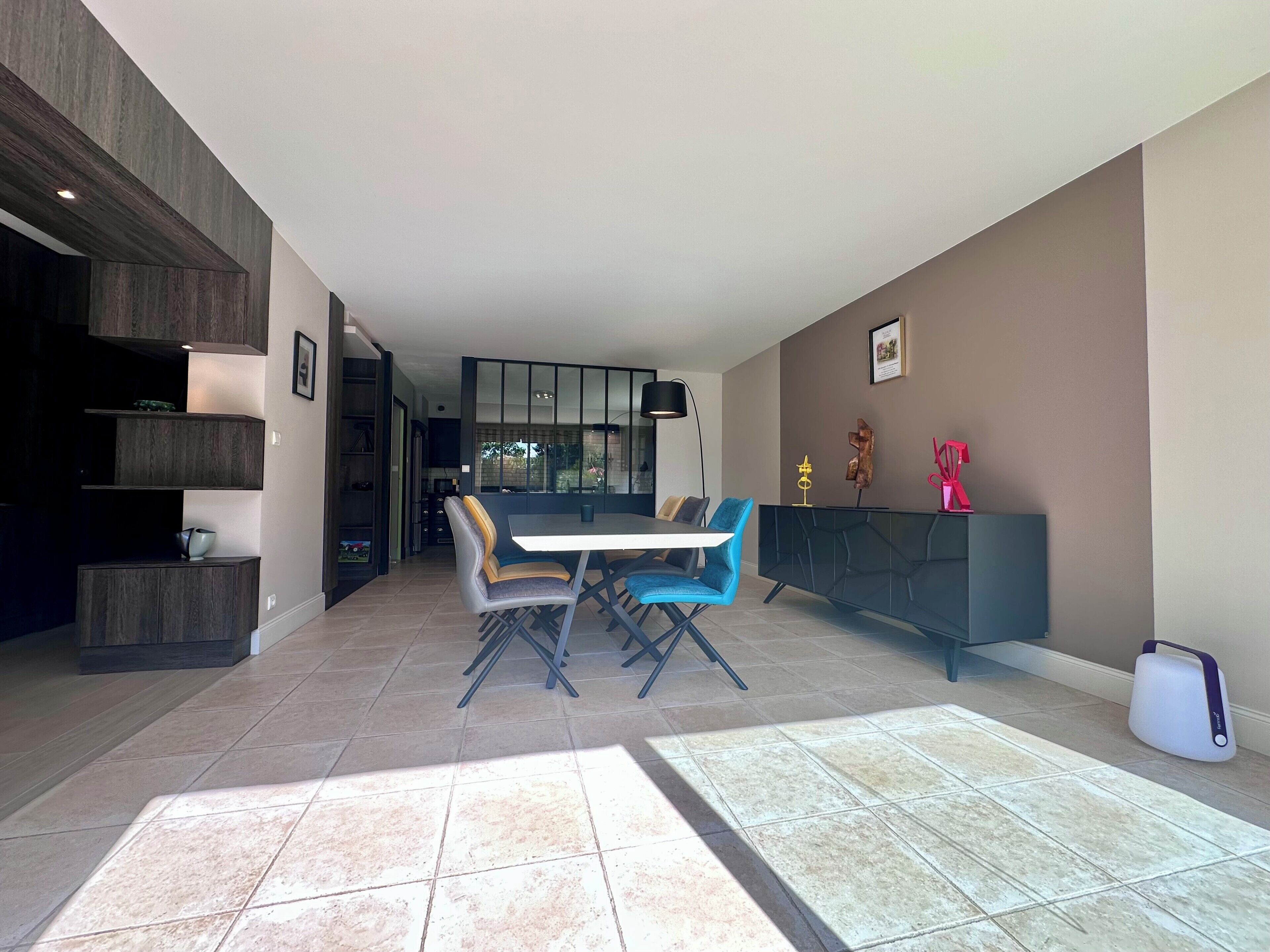 Un espace repas moderne avec une table et des chaises, une étagère en bois foncé et une cuisine en arrière-plan.
