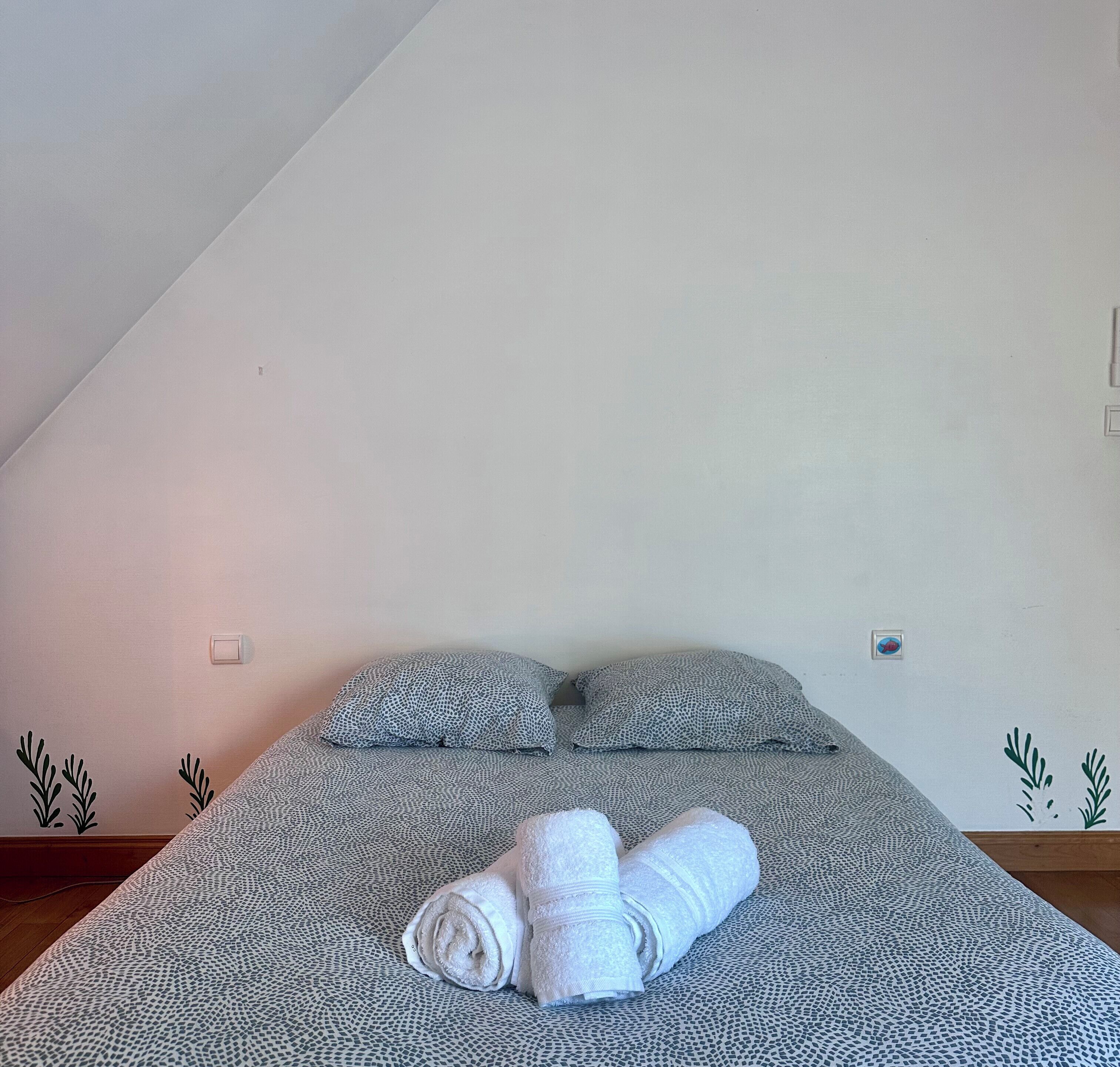 Un dormitorio con cama, almohadas y una toalla enrollada.