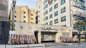 Ein Hotel mit Eingangsbereich und einem Schild mit der Aufschrift "FILM HOTEL". Vor dem Eingang stehen Blumenarrangements.