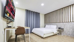 Ein Hotelzimmer mit Bett, Schreibtisch, Stuhl, Wandfernseher und Vorhang.
