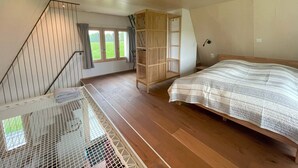 Ein Schlafzimmer mit einem hölzernen Bett, einer Treppe mit Metallgeländer, einem Holzschrank und einem Fenster mit Vorhängen.