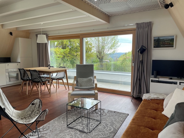A modern living room with a sofa, a glass coffee table, and a dining area with chairs and a table. - Beautiful holiday home surrounded by nature (Les Enfers)