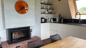 A kitchen with a fireplace, a dining table, and a window. - Beautiful holiday home surrounded by nature (Les Enfers)