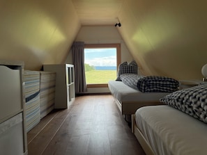 A bedroom with a sloped ceiling, a bed with checkered bedding, a bedside table, and a window with a view of a green field. - Beautiful holiday home surrounded by nature (Les Enfers)