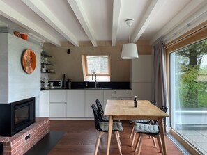 A modern kitchen with a built-in oven, a dining area with a wooden table and chairs, and a window with a view of greenery. - Beautiful holiday home surrounded by nature (Les Enfers)