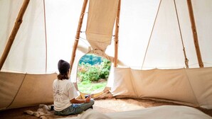A person sitting inside a tent with a view of greenery outside. - Shanti Tipi 3 Summary (Tintagel)