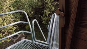 Un banc en métal installé à l’extérieur, doté d’une rambarde en métal, d’une porte en bois et offrant une vue sur la verdure en arrière-plan.