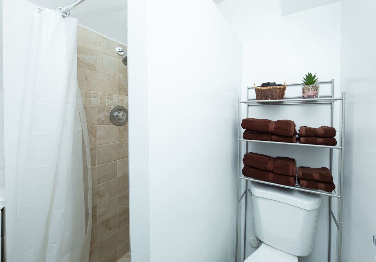 Een badkamer met een douche, toilet en een plank met handdoeken en een plant.