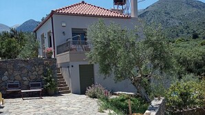 A stone-paved courtyard leading to a building with a tiled roof, surrounded by greenery and mountains in the background. - Villa Kastania, Melidoni, Chania, Crete. (Melidoni Chania)