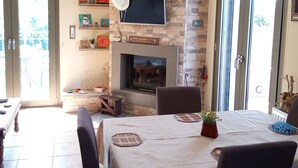 A dining area with a stone fireplace, a television mounted above it, and a table set for four. - Villa Kastania, Melidoni, Chania, Crete. (Melidoni Chania)