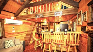 Interior acogedor de una cabaña con una zona de bar de madera, un sofá y una escalera que sube a un nivel superior.