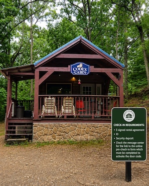 A cabin with a stone foundation, a porch with chairs, and a sign listing check-in requirements. - Codex Cabin (Murfreesboro)