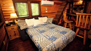 Un dormitorio acogedor de estilo cabaña, con una cama, una mesita de noche, un tocador, un ventanal con persianas y una escalera que lleva a una zona de altillo.