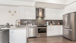 A modern kitchen with white cabinets, a stainless steel refrigerator, a built-in oven, and a backsplash with gray tiles. - Holiday retreat in Toronto (Toronto)