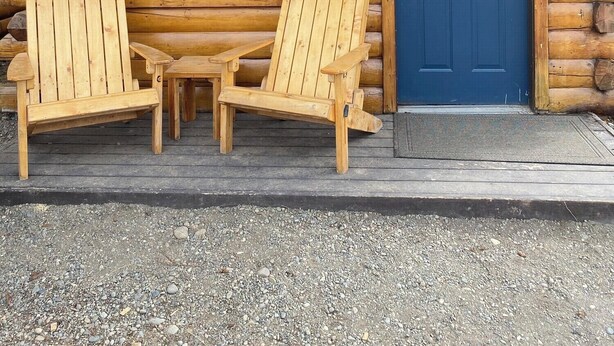 A log cabin with two wooden Adirondack chairs outside, a blue door, and a window with a view of a car and trees. - Angler Cabin-Modern Comfort in the Last Frontier (For families or casual travelers) (Tok)