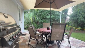 Un patio al aire libre con una parrilla, una mesa con sillas y un gran paraguas.