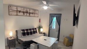 Un dormitorio con cama, mesitas de noche, un escritorio, ventilador de techo, ventana con cortinas y televisor montado en la pared.