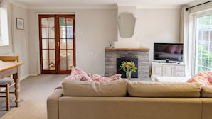 Een woonkamer met een bank, een televisie, een open haard en een deur naar een andere kamer.