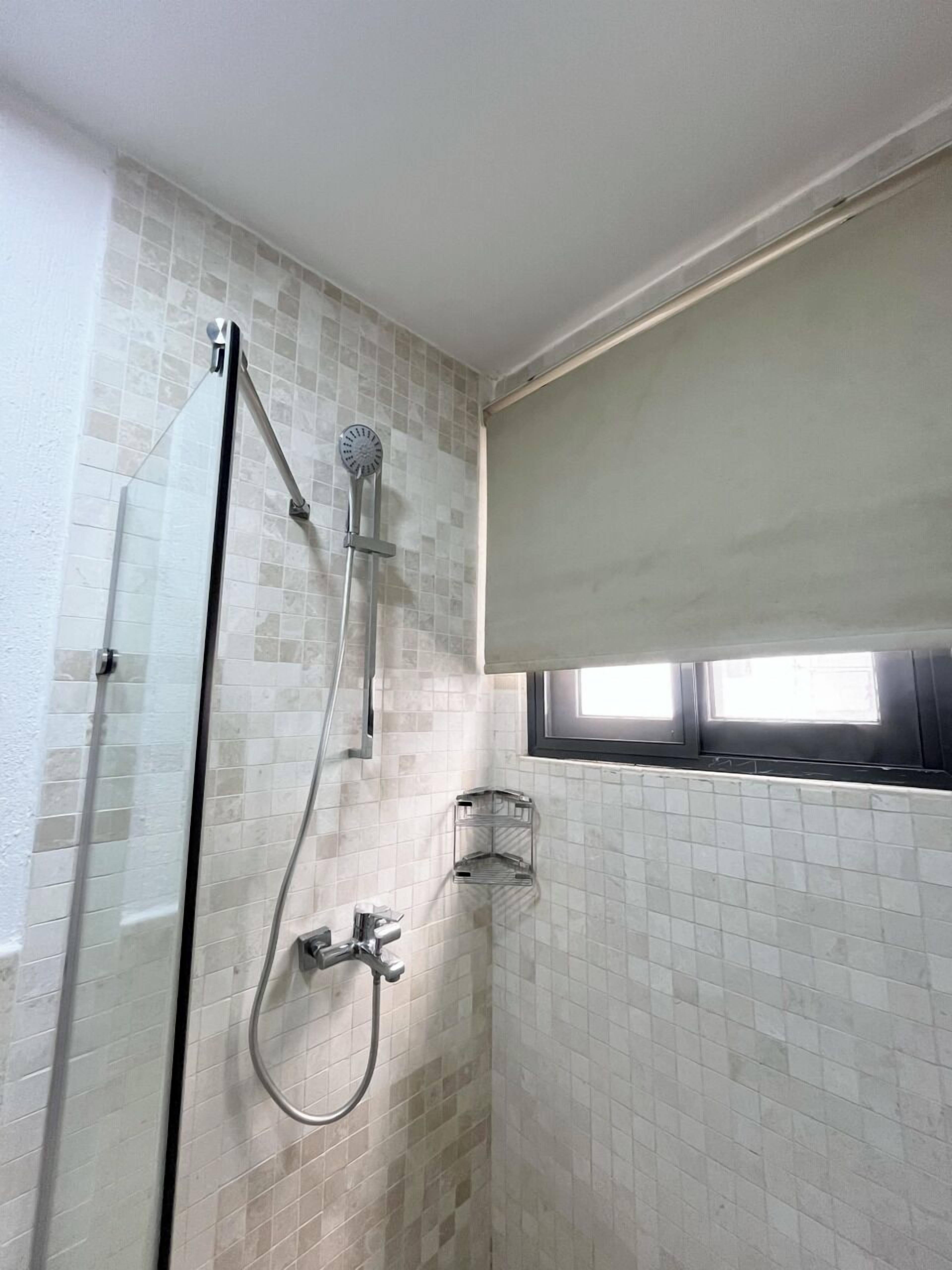A shower with a glass door, a handheld showerhead, and a wall-mounted faucet.