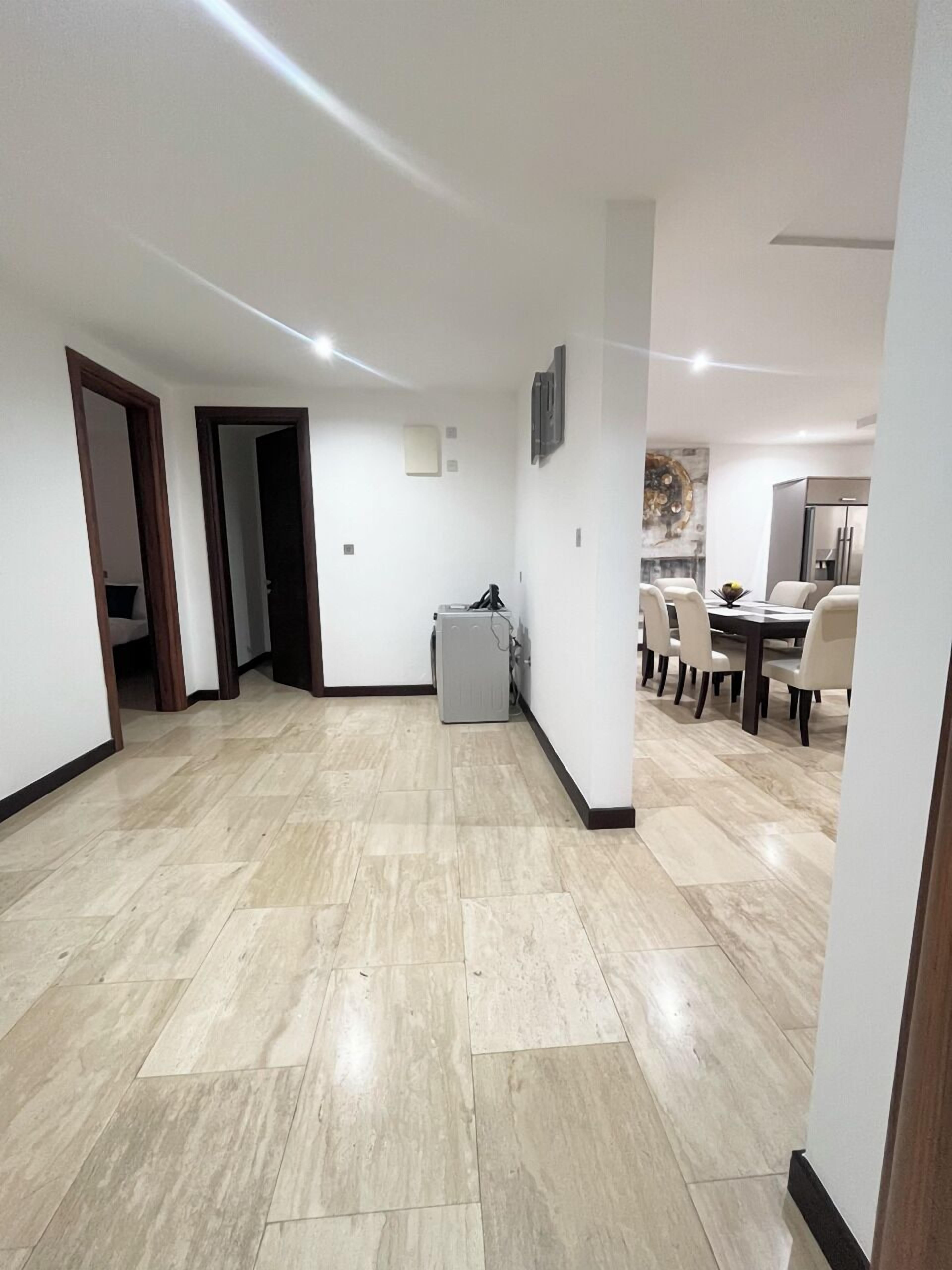 A spacious living area with a dining table and chairs, a small kitchenette, and a door leading to another room.