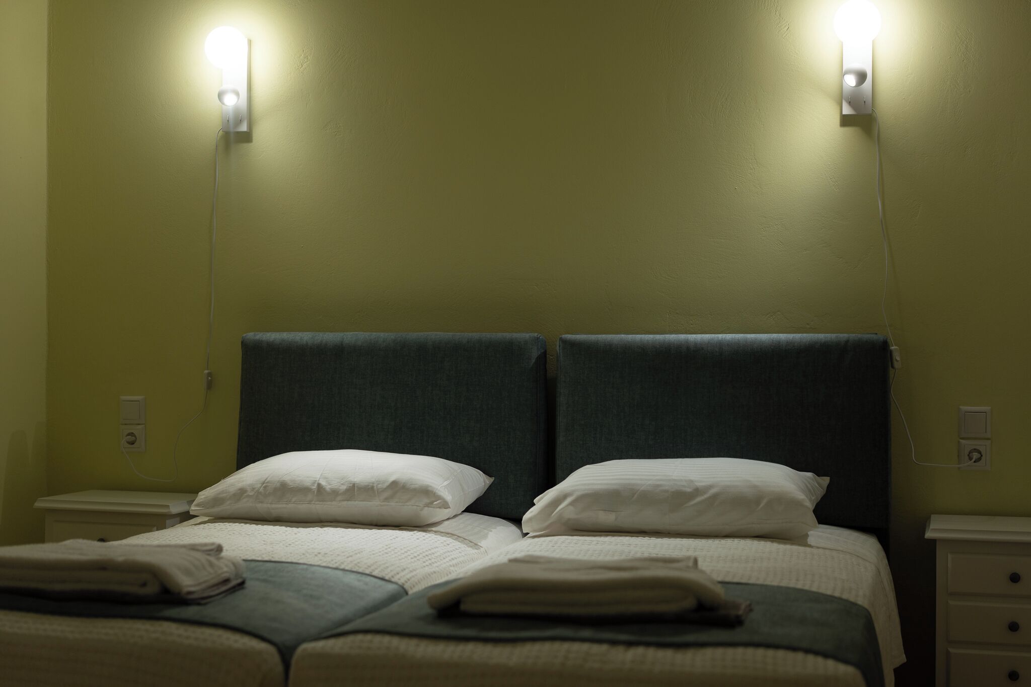 Una cama doble con dos almohadas, una mesita de noche y una lámpara de pared.