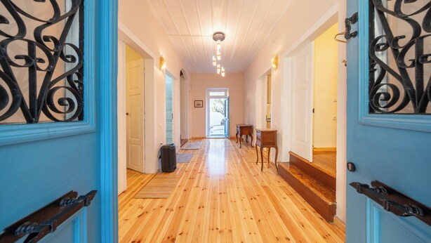 A hallway with wooden flooring, a ceiling light, and a door with a decorative metal design. - Eleofilos Old Town (Lesvos)