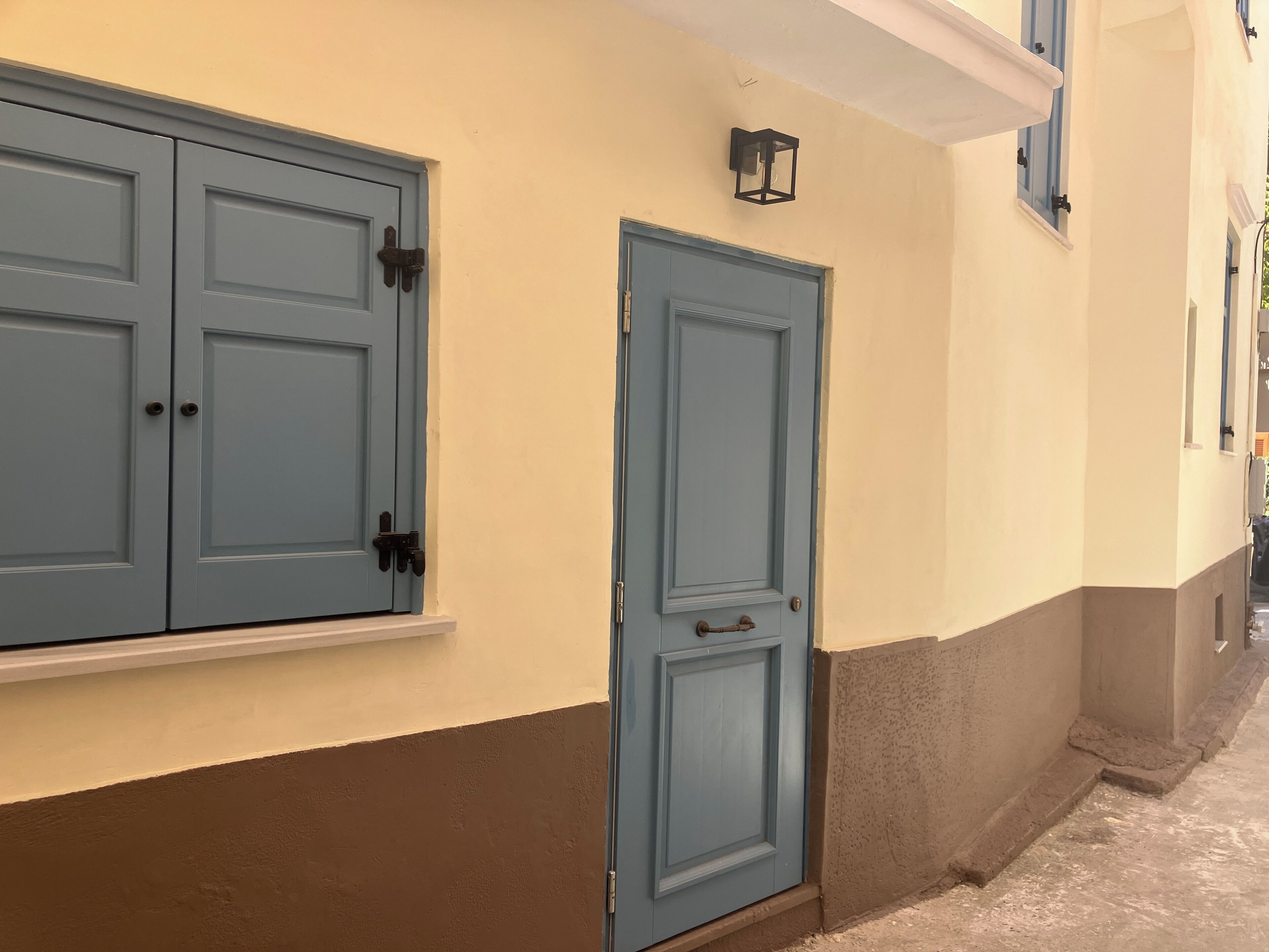 A building with two blue doors, a light fixture, and a window with blue shutters.