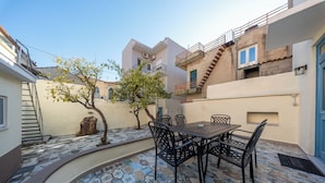 A courtyard with a tiled patio, a table with chairs, a tree, and a staircase leading to a balcony. - Eleofilos Old Town (Lesvos)