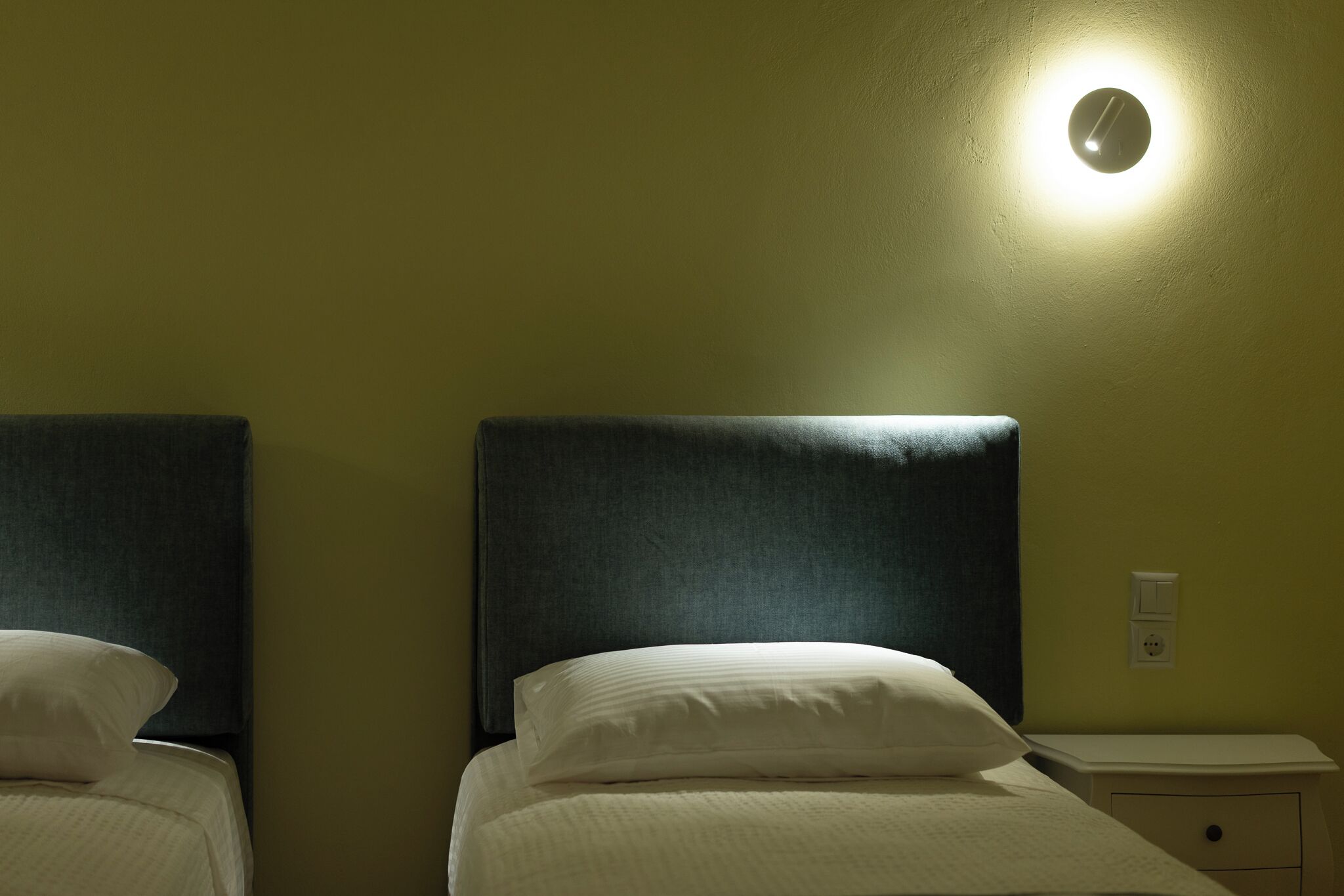 A hotel room with two beds, a nightstand, and a wall-mounted light fixture.