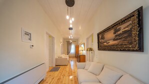 A hallway with a wooden floor, white walls, a white sofa, a painting, and a ceiling light fixture. - Eleofilos Old Town (Lesvos)