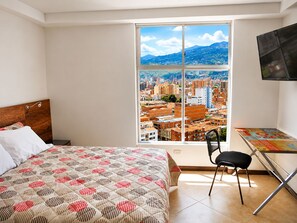 A hotel room with a bed, a desk, a chair, and a large window offering a city view. - penthouse jacuzzi rooftop fun in the sun (Medellín)