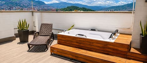 A rooftop terrace with a wooden deck, a hot tub, and two lounge chairs.